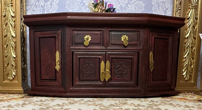 May include: A dark wood jewelry box with intricate carvings and brass hardware. The box has two doors with brass handles and two drawers with brass knobs.