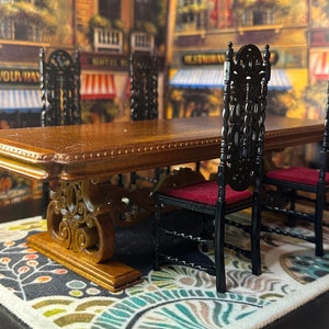May include: A miniature dining set comprising a wooden table with decorative legs and four black chairs with red cushions. The table sits on a patterned rug. The background shows a European street scene.