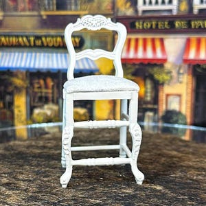 May include: White wooden chair with a carved back and a white cushion. The chair has a step stool and is in a dollhouse setting.