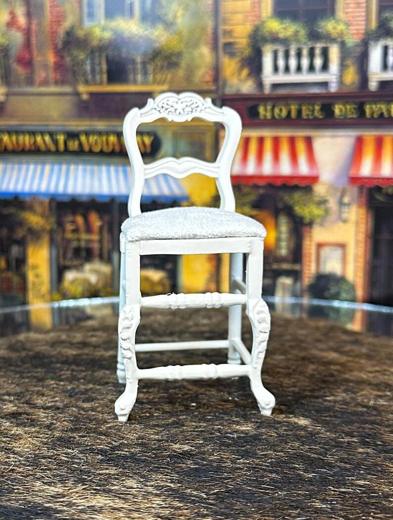 May include: White wooden chair with a carved back and a white cushion. The chair has a step stool and is in a dollhouse setting.