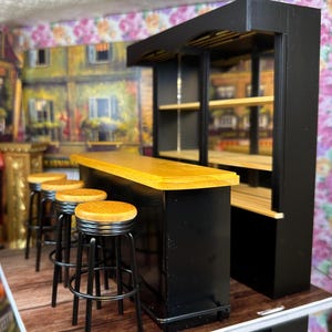 Puede incluir: Un conjunto de bar negro en miniatura con una encimera de madera y estantes. La barra tiene cuatro taburetes de bar de metal negro con asientos marrones.