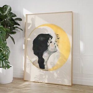 May include: A framed art print featuring a woman and a crescent moon in a romantic embrace. The artwork is in a vintage style, with the woman's silhouette in black and the moon in yellow. The frame is a light wood color.