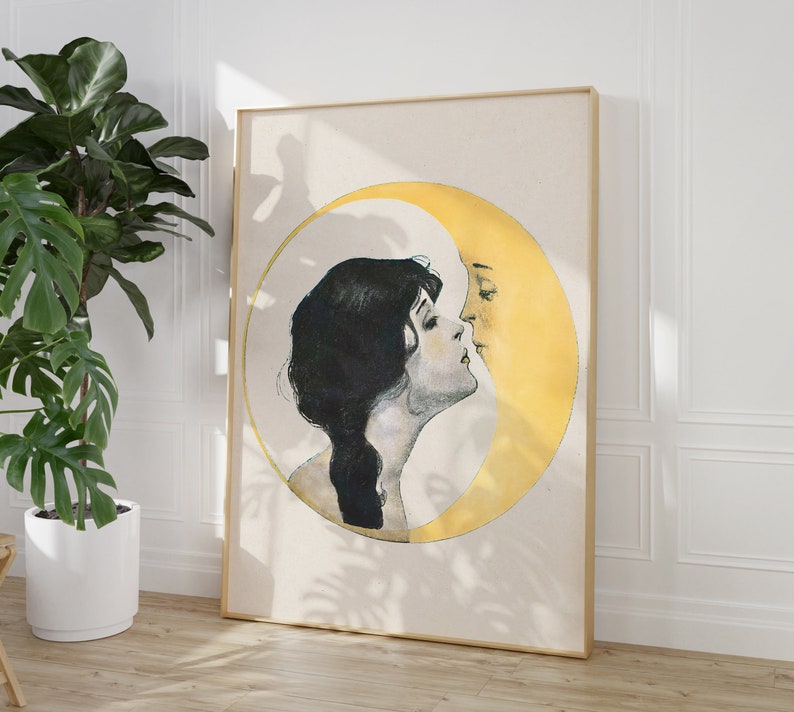 May include: A framed art print featuring a woman and a crescent moon in a romantic embrace. The artwork is in a vintage style, with the woman's silhouette in black and the moon in yellow. The frame is a light wood color.