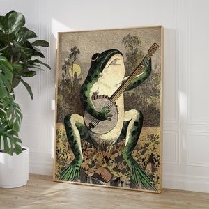 May include: A green frog playing a banjo with a brown wooden body and white strings. The frog is sitting on a brown and green background with leaves and flowers.