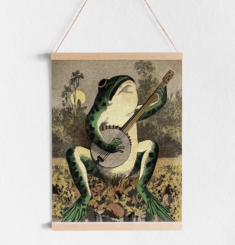 May include: A green frog playing a banjo with a brown wooden body and white strings. The frog is sitting on a bed of green and brown leaves. The background is a blurry image of trees and a moon.