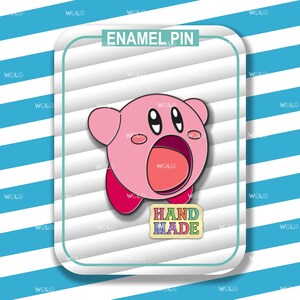 K&ouml;nnte beinhalten: Rosa emaillierte Anstecknadel mit einem Cartoon-Charakter mit einem gro&szlig;en, offenen Mund. Der Charakter hat gro&szlig;e Augen und einen rosa K&ouml;rper. Die Anstecknadel tr&auml;gt die Aufschrift "HAND MADE" in Regenbogenfarben.
