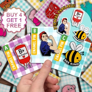 Pode incluir: Três pinos de esmalte que representam uma bolsa de sangue com o texto "B+ Be Positive", uma mulher com um lenço vermelho em uma pose "We Can Do It" e uma abelha amarela e preta com o texto "Bee Kind". Os pinos estão sobre um fundo xadrez com o texto "ENAMEL PIN" e "BEE KIND" em cada cartão.