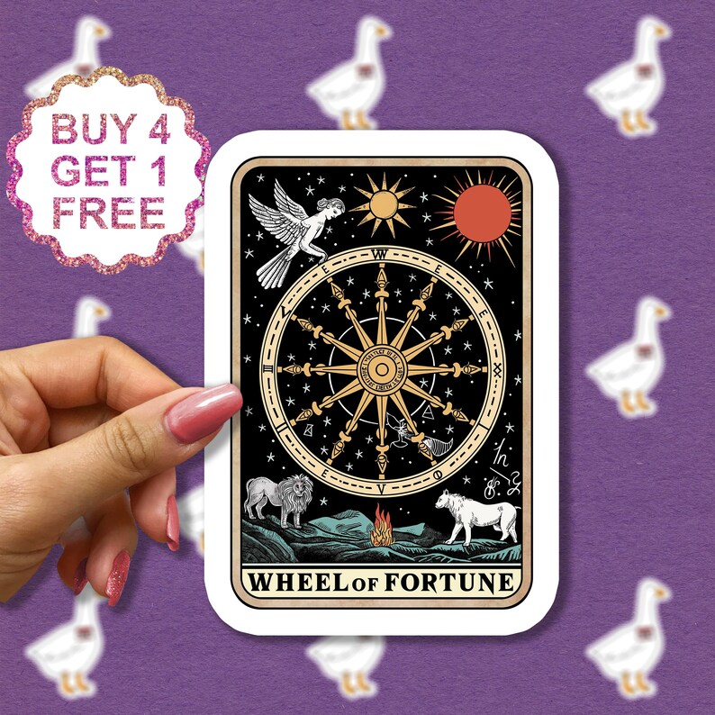 May include: A tarot card sticker featuring the Wheel of Fortune card. The card is illustrated with a wheel with eight spokes, a lion, a wolf, and a sphinx. The card is set against a black background with stars and a sun and moon.