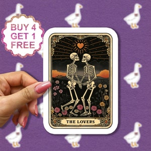May include: A tarot card with a black background and a gold frame. The card depicts two skeletons holding hands and looking at each other. The card is titled "The Lovers".