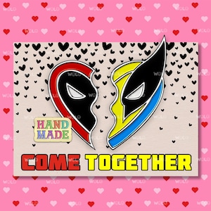 Op de afbeelding: Twee halve hartvormige pinnen, een rood en zwart, de andere geel en blauw, met de tekst "COME TOGETHER" eronder. De pinnen bevinden zich op een bruine achtergrond met zwarte harten. Een klein bordje staat "HAND MADE".
