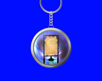 Puede incluir: Un llavero redondo plateado con un dije transparente en forma de burbuja. Dentro del dije hay una imagen rectangular de color beige con una cara, sobre un fondo colorido y arremolinado. El llavero tiene una cadena plateada y un fondo azul.