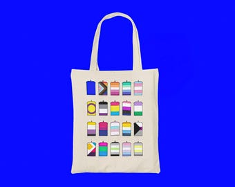 May include: A beige canvas tote bag featuring a grid of twenty rectangular icons, each displaying a different colorful pride flag pattern. The bag has two long shoulder straps and is centered against a solid, bright blue background.