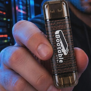 May include: A black USB flash drive featuring a binary code pattern of ones and zeros printed on the surface. The device displays the white text Bootable USBs with a graphic icon of a flash drive. It has a translucent dark brown cap.