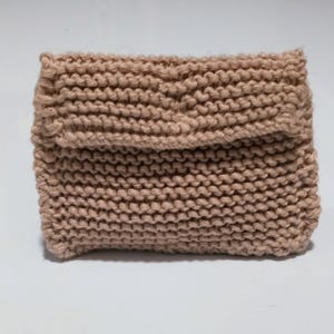 May include: A light brown knitted pouch with a folded flap. The pouch is made of a soft, textured yarn.