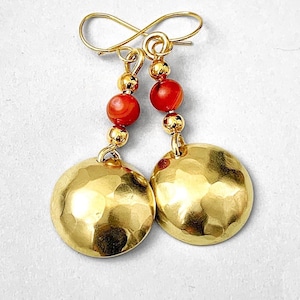May include: Gold-tone earrings with a hammered disc design. The earrings feature red beads and gold-coloured accents. The earrings are suspended from a gold-coloured hook.