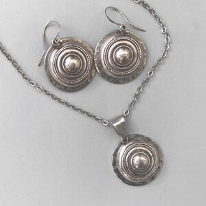 Domed silver earrings with hammered base and raised centre, shown on a grey background.