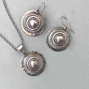 Domed silver earrings with hammered base and raised centre, shown on a grey background.