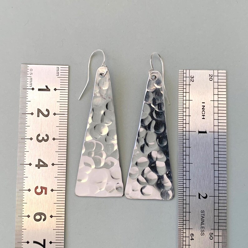 Hammered triangle earrings next to two rulers to show length in cm and inches