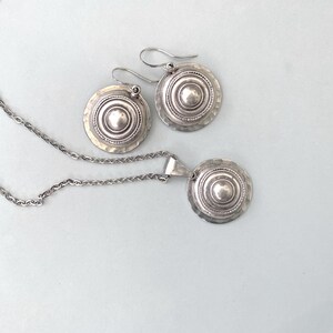 Domed silver earrings with hammered base and raised centre, shown on a grey background.