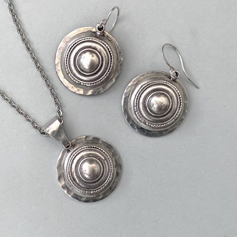 Domed silver earrings with hammered base and raised centre, shown on a grey background.