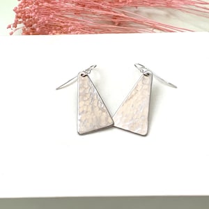 May include: A pair of silver triangle earrings with a hammered texture and a white finish.