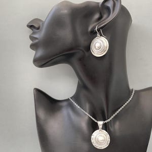 Convex coin-shaped silver earrings shown on a mannequin head to show size and shape.