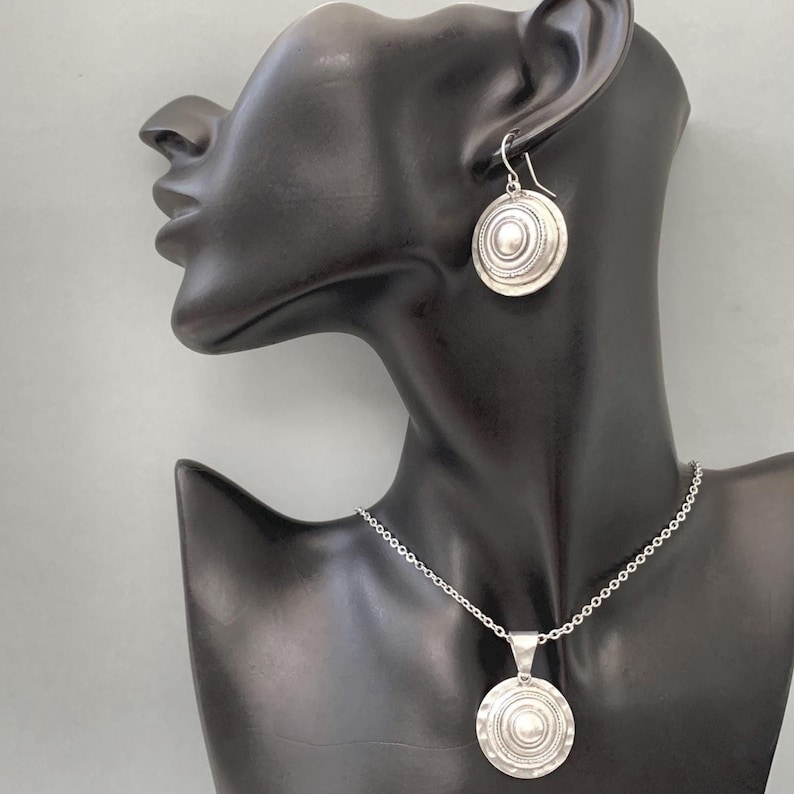 Convex coin-shaped silver earrings shown on a mannequin head to show size and shape.