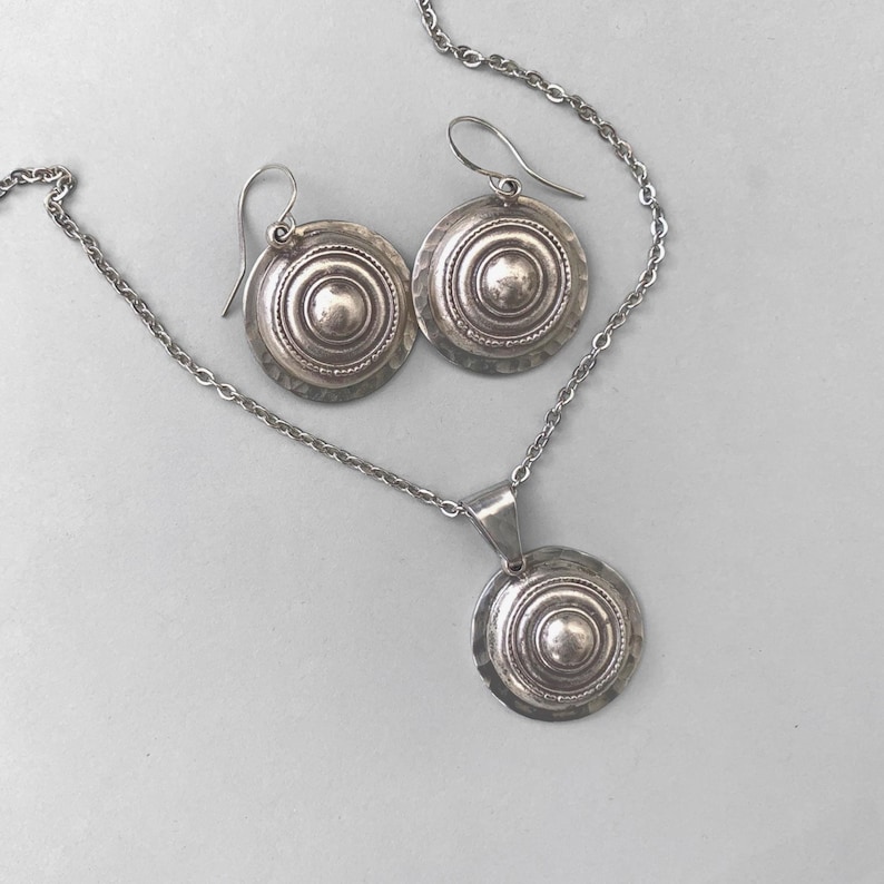 Domed silver earrings with hammered base and raised centre, shown on a grey background.