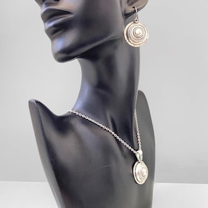 Convex coin-shaped silver earrings shown on a mannequin head to show size and shape.