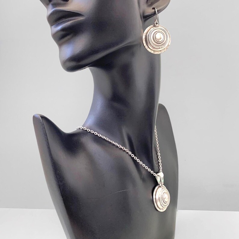 Convex coin-shaped silver earrings shown on a mannequin head to show size and shape.
