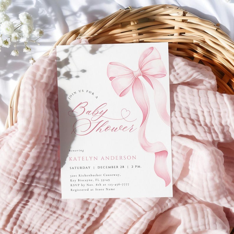 May include: A baby shower invitation with a watercolor pink bow and ribbons. The invitation reads "Join us for a Baby Shower" and includes event details. The invitation is on a white background.