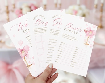 May include: Four pink and white bridal shower game cards. Each card features a different game, including "Bridal Shower Bingo" and "Bride's Phrase." The cards are decorated with pink watercolor illustrations of champagne glasses and pink floral accents.