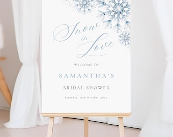 May include: A white sign on a wooden easel. The sign has the text "Snow in Love" and "Welcome to Samantha's Bridal Shower". It features blue snowflake designs and the date Saturday, 28th October, 2025.