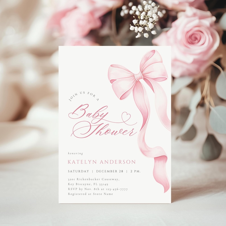 May include: A baby shower invitation with a soft pink bow and flowing ribbons. The invitation text reads "Join us for a Baby Shower" in elegant script. Details include the honoree's name, date, time, and location.