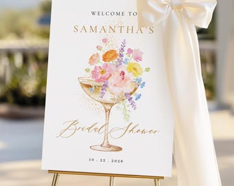 May include: A white welcome sign on a gold easel, featuring the text "WELCOME TO SAMANTHA'S Bridal Shower" in gold script. A champagne glass filled with colorful flowers is the central design element. The date "10.22.2026" is at the bottom.