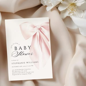May include: A pink baby shower invitation with a large pink bow in the center. The text reads "Join us for a Baby Shower in honor of Stephanie Williams, October 28th, 2023 at 3:00 PM, 3101 Rickenbacker Causeway, Key Biscayne, FL 33149, RSVP by July 8th at 123-456-7777, Registered at Company Name."