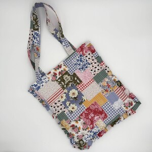 May include: A patchwork tote bag with floral, gingham, and striped fabric squares in shades of red, pink, blue, green, and yellow. The bag has matching fabric handles and a label that reads "Flip the bra".