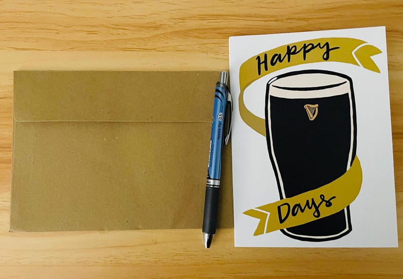 May include: A white card with the text "Happy Days" in black script. The card features a gold ribbon with a black glass of beer with a gold harp logo.