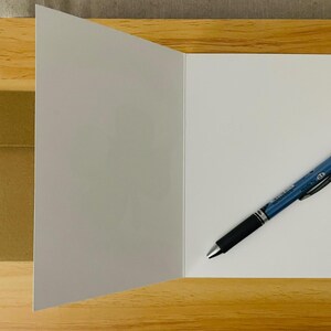 May include: A blank white card with a brown envelope and a blue pen on a wooden surface.