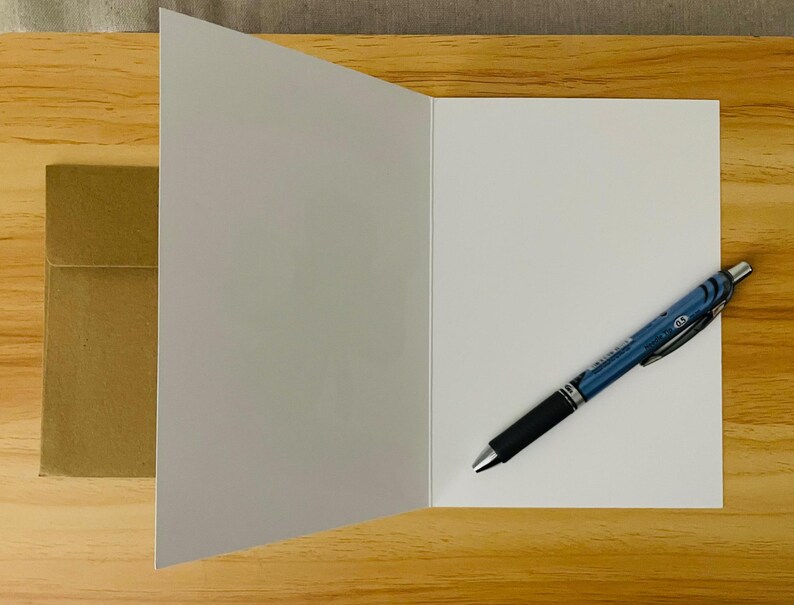 May include: A blank white card with a brown envelope and a blue pen on a wooden surface.