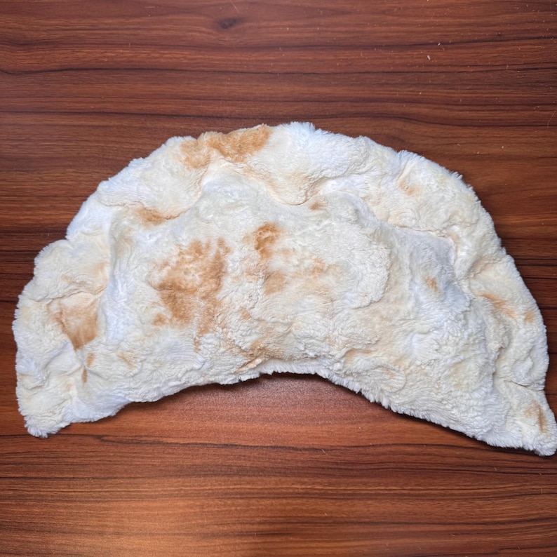 May include: A plush, half-moon shaped pillow in off-white with brown patches, resembling a pita bread. The soft, textured surface gives the pillow a cozy appearance. This decorative pillow is ideal for home decor.