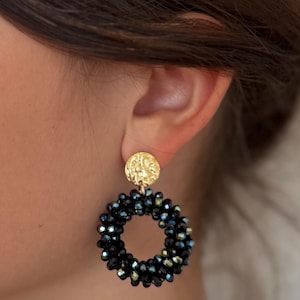 Könnte beinhalten: Goldfarbene Ohrstecker mit strukturiertem, kreisförmigem Design. Die Ohrringe haben einen kreisförmigen Reifen aus kleinen, dunkelblauen und irisierenden Perlen. Ein stilvolles Accessoire.