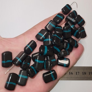 May include: A collection of rectangular black beads, each featuring a single horizontal teal stripe. The beads are shown alongside a metal ruler, indicating a length of approximately 18 millimetres for each individual bead piece.