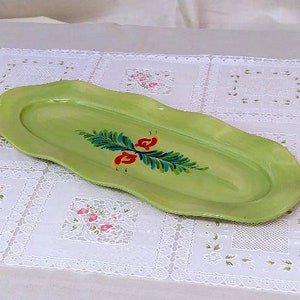 May include: A light green oval serving dish with a hand-painted floral design in red, blue, and green. The dish has a scalloped edge and is perfect for serving snacks or appetizers.