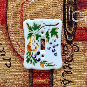 May include: A white ceramic light switch cover with a hand-painted design of grapes and leaves in shades of green, yellow, and purple.