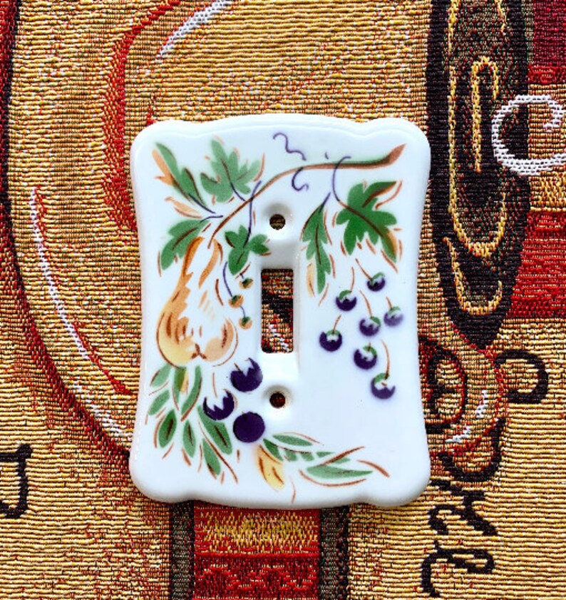 May include: White ceramic light switch cover with a hand-painted design of green leaves, yellow pears, and purple berries.