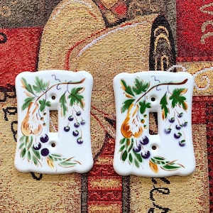 May include: Two white ceramic light switch covers with a pear and berry design. The design features a pear branch with green leaves, yellow pears, and purple berries.