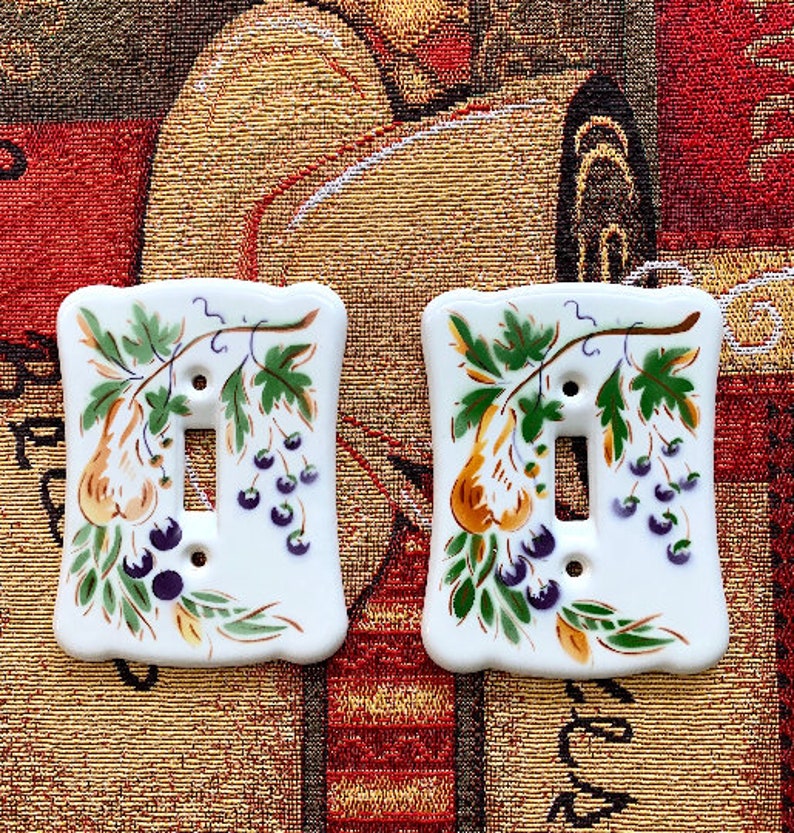 May include: Two white ceramic light switch covers with a pear and berry design. The design features a pear branch with green leaves, yellow pears, and purple berries.