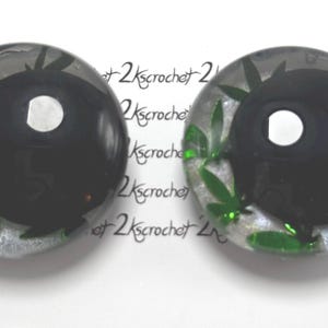 Peut inclure: Deux cabochons ronds en r&eacute;sine transparente avec un motif yin-yang noir. Le motif est orn&eacute; de feuilles de cannabis vertes. Le fond est un glitter argent&eacute;. Le texte "2kscrochet" est r&eacute;p&eacute;t&eacute; autour des cabochons.