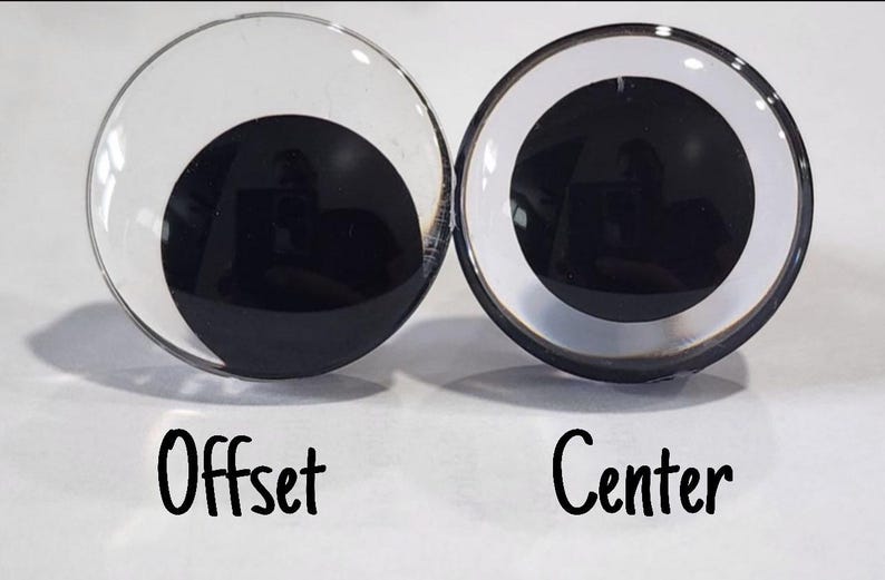 May include: Two plastic googly eyes, one with the pupil centered and the other with the pupil offset. The eyes are clear with a black pupil and a white ring around the pupil.
